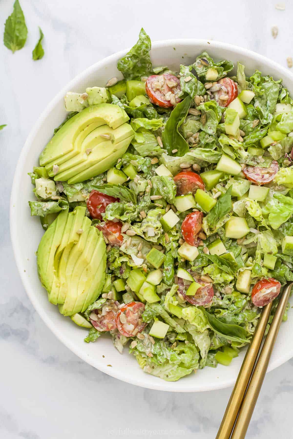 Featuring crisp lettuce, juicy cucumber, crunchy green pepper & more, this easy Green Goddess Salad is an ultra-satisfying appetizer or side. A pair of golden chopsticks digging into a bowl of green goddess salad