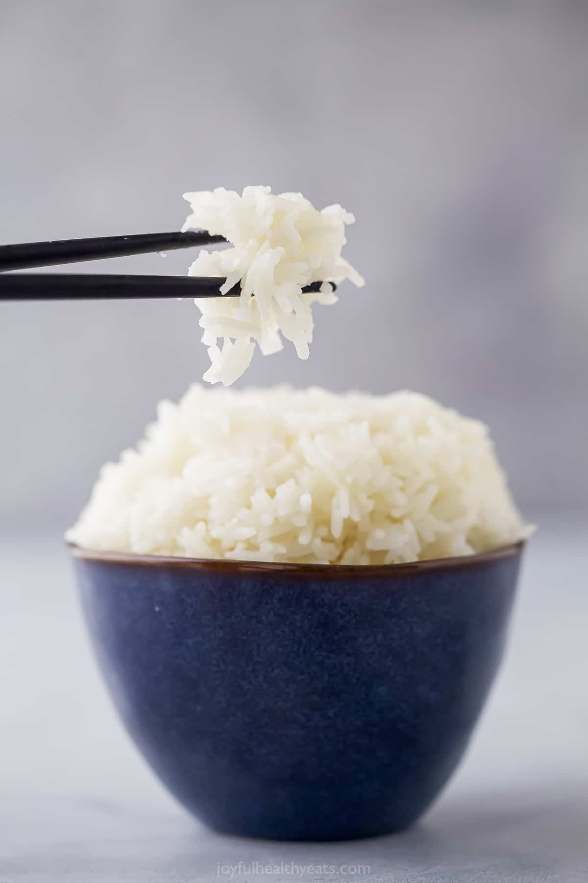 This Instant Pot Jasmine Rice recipe shows you how to cook perfectly tender and fluffy rice. It only takes a few minutes to make! a small blue bowl with cooked white rice and chopsticks taking a bit out
