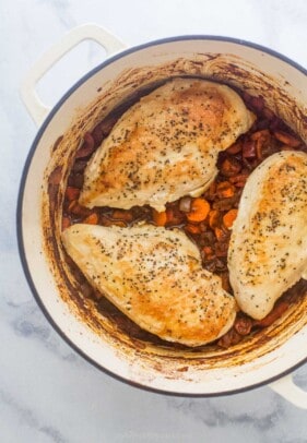 Three chicken breasts cooked in a large pot with vegetables and a tomato based sauce.