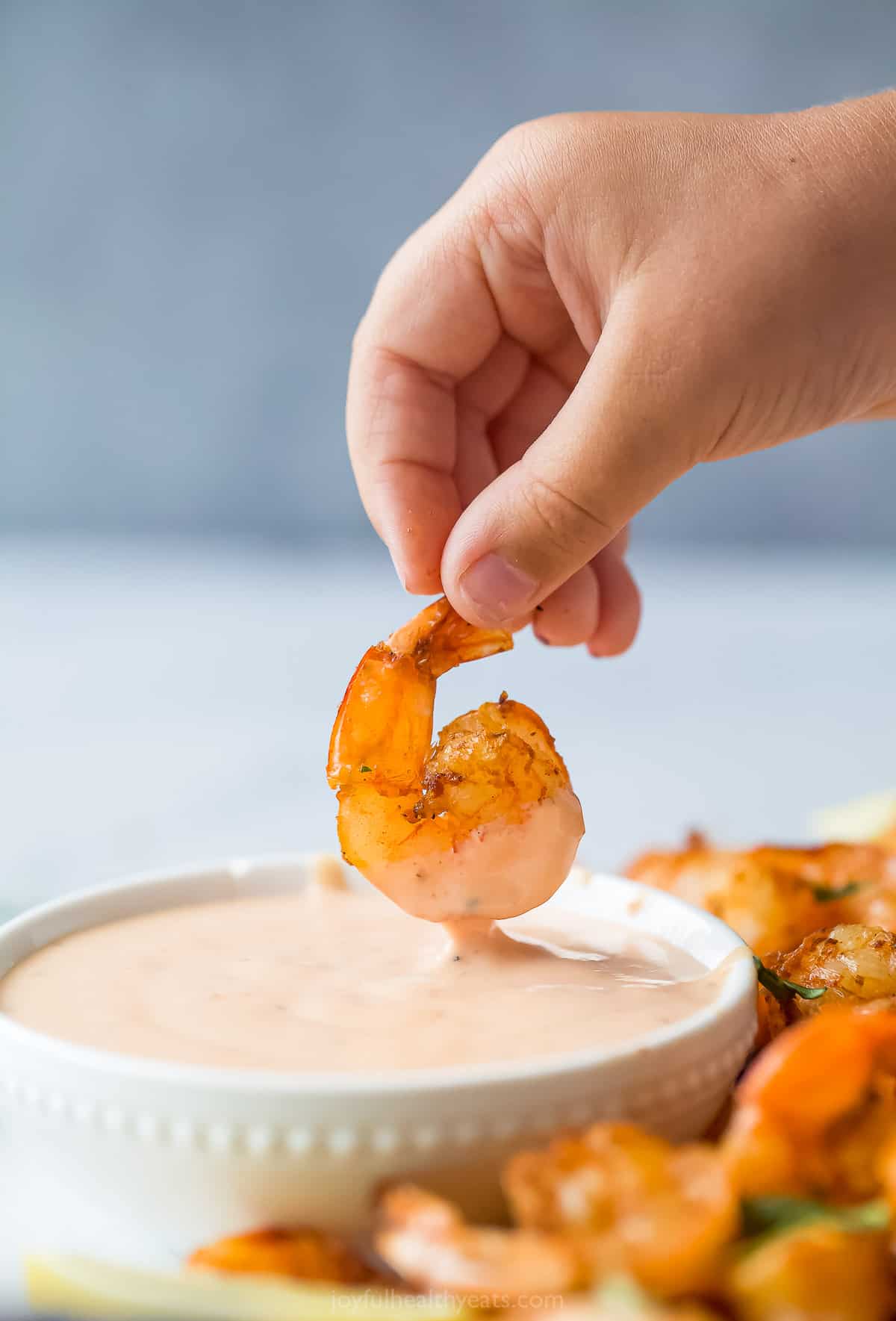 Here's how to make Boom Boom Sauce right at home. This super easy sauce is made with mayo, chili sauce, ketchup, and sriracha. someone dipping shrimp into a pale red dipping sauce