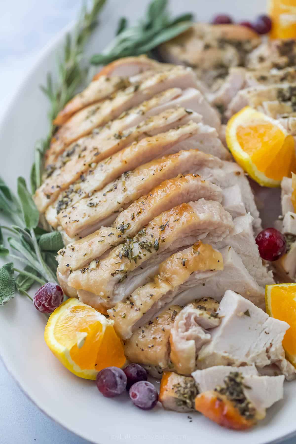 This Roasted Turkey Breast recipe is seasoned with garlic and herb compound butter. It comes out juicy, tender, and with so much flavor! roasted turkey breast that's been sliced on a plate with herbs and orange wedges
