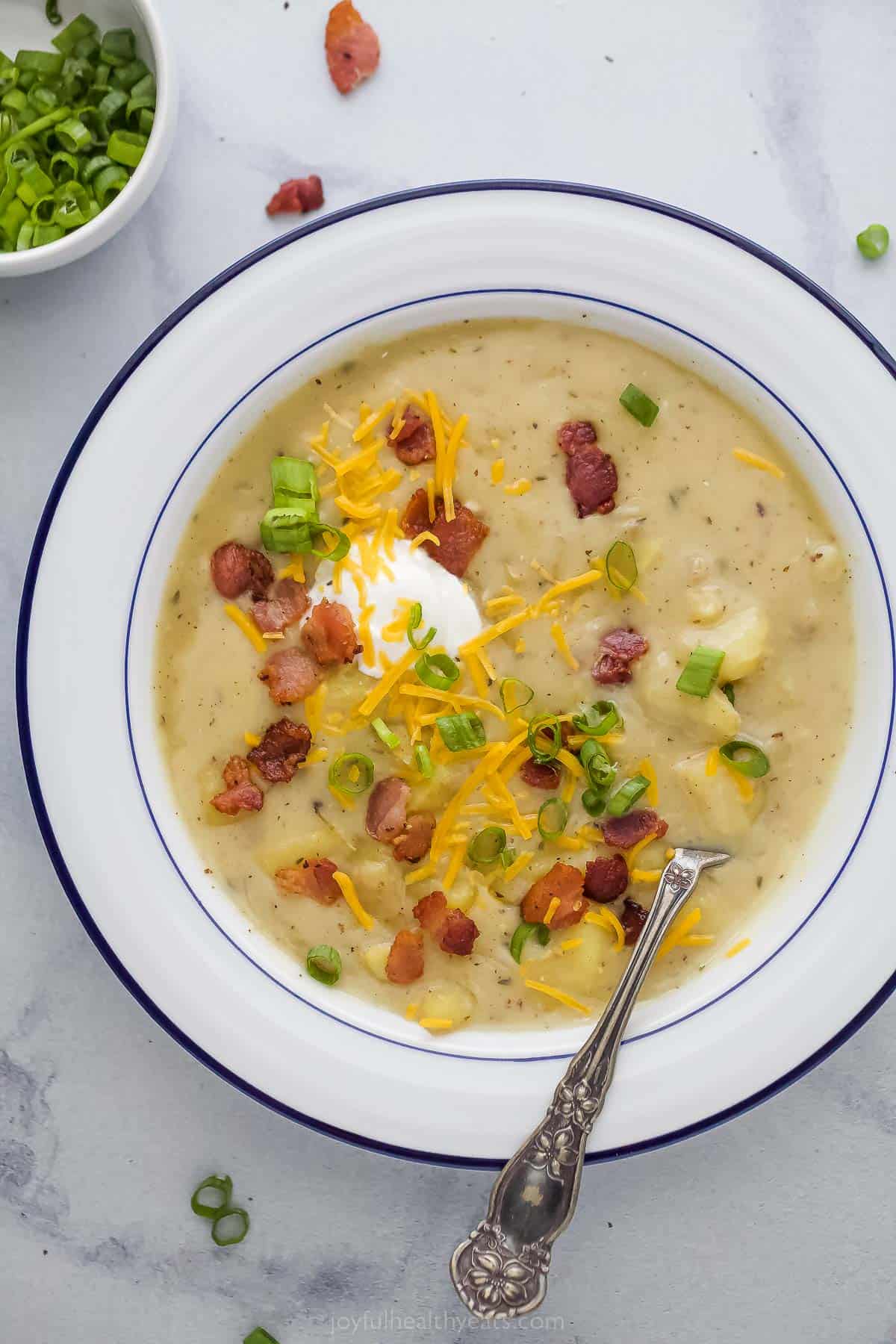 This Instant Pot Potato Soup is rich, creamy, and the perfect comfort food. Top it with cheese, crumbled bacon, and sour cream! a bowl of creamy potato soup with bacon and cheese garnish