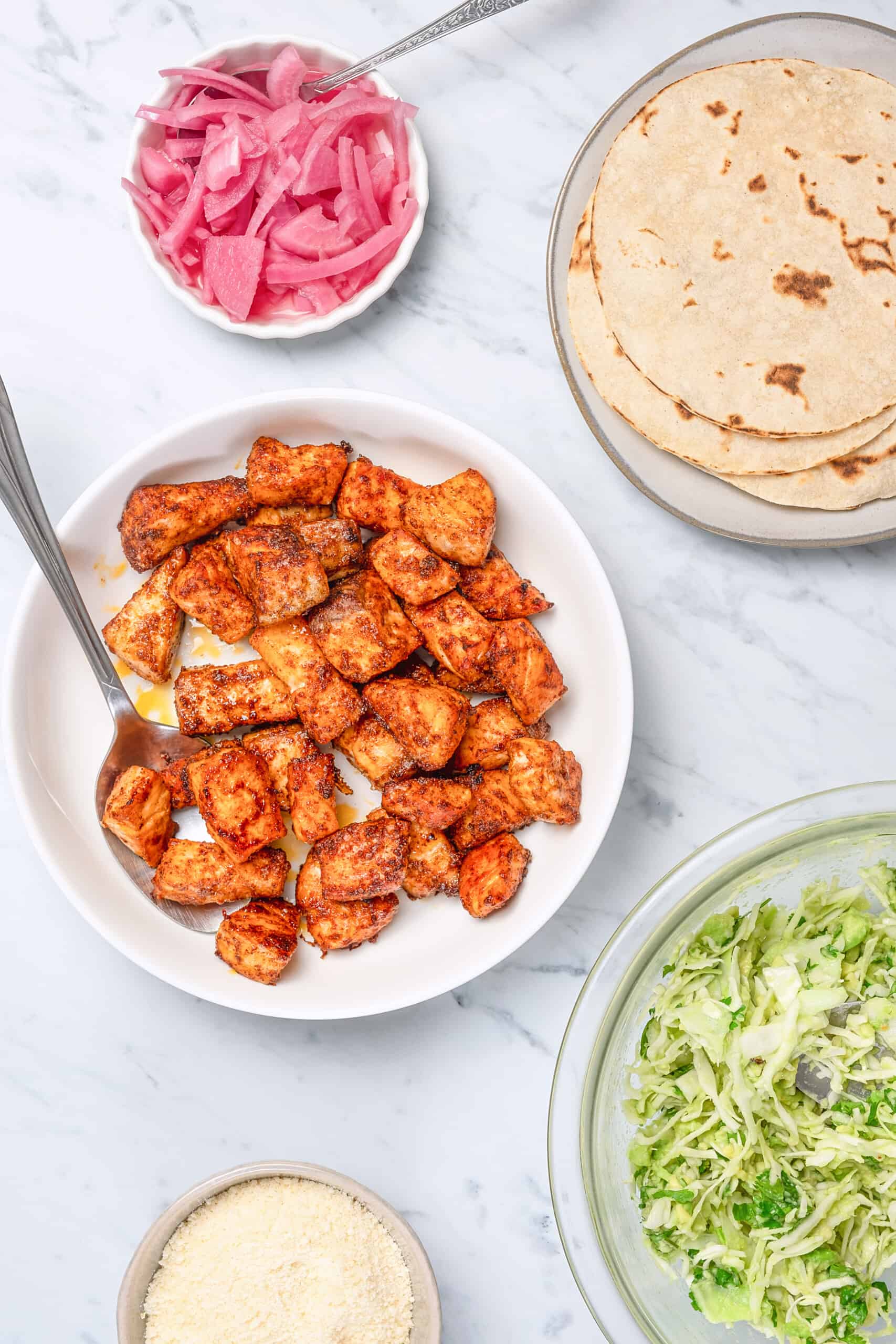 Cooked salmon in a bowl alongside tortillas and slaw.