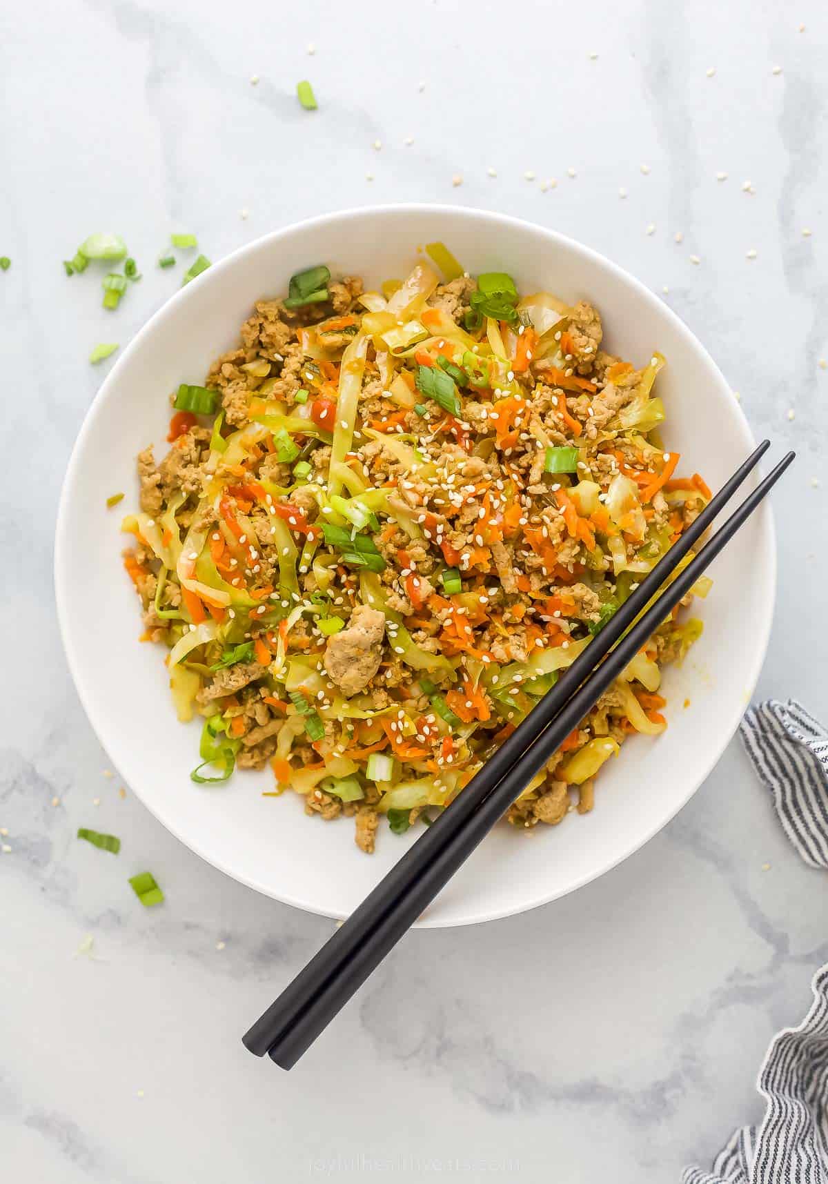 Egg Roll in a Bowl is an easy and healthy dinner that's ready in 20 minutes. It has ground turkey, cabbage, carrots, and sweet soy sauce. egg roll in a bowl plated in a white bowl which is ground turkey, cabbage, and carrots tossed a soy-based sauce