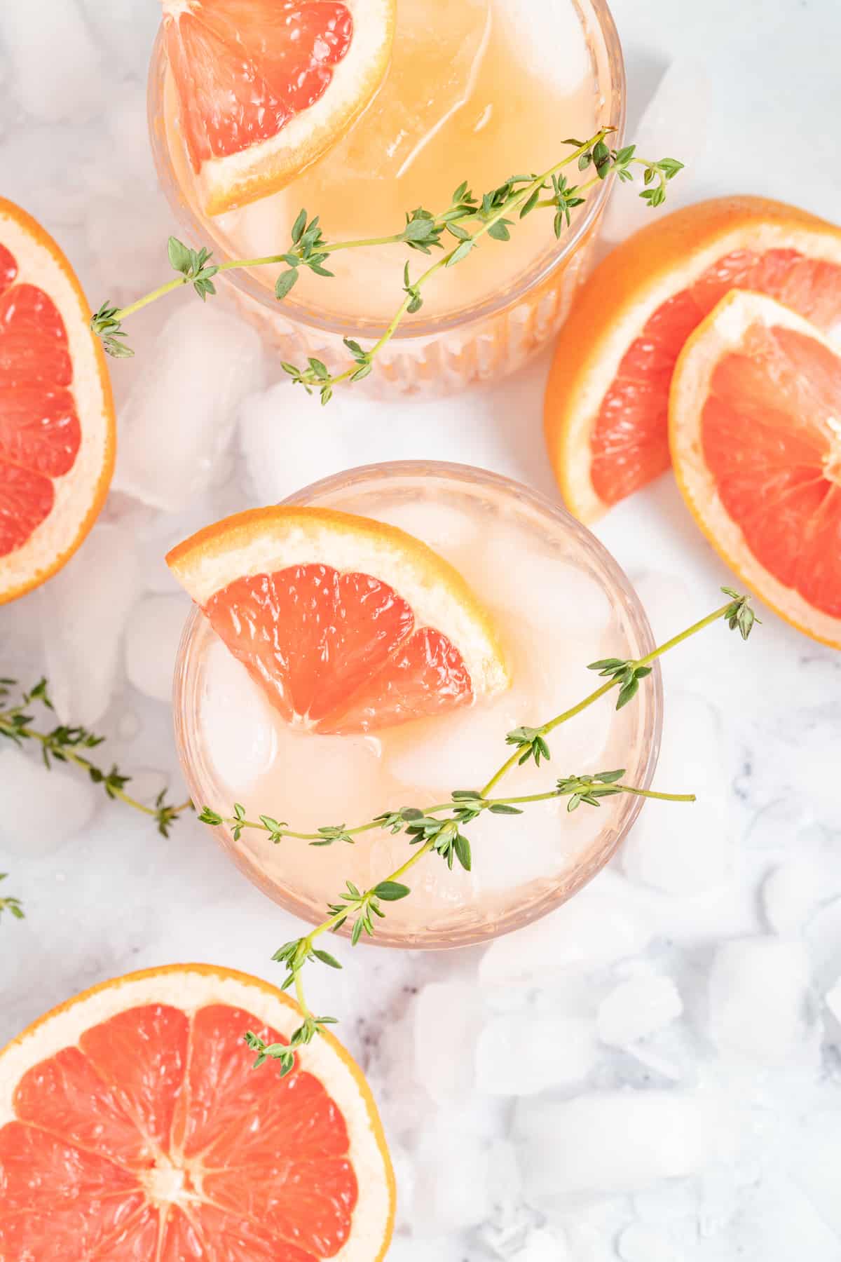This tangy and refreshing Greyhound Cocktail is made with just 3 ingredients. It has fresh grapefruit juice, vodka, and some bubbles! top view of a grapefruit cocktail with a grapefruit wedge and fresh herb garnish