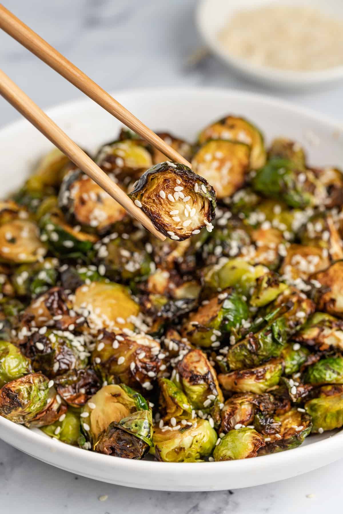 These Crispy Asian Air Fryer Brussels Sprouts are crunchy little bites filled with lots of soy, ginger, garlic, and spicy flavor. a bowl of crispy fried brussels sprouts