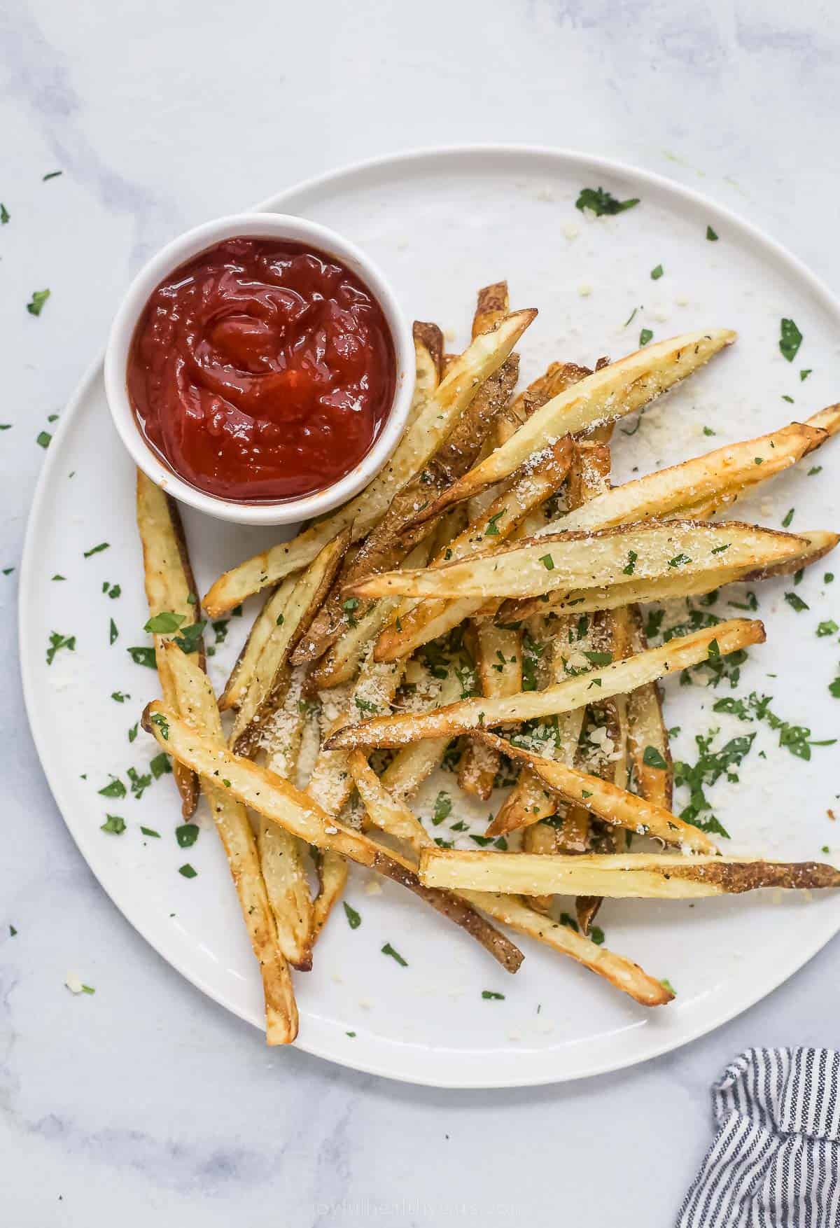 Thinly sliced and ultra crispy, these homemade pommes frites with parmesan and fresh parsley are the perfect French comfort food. Pommes frites on a plate with ketchup on the side.
