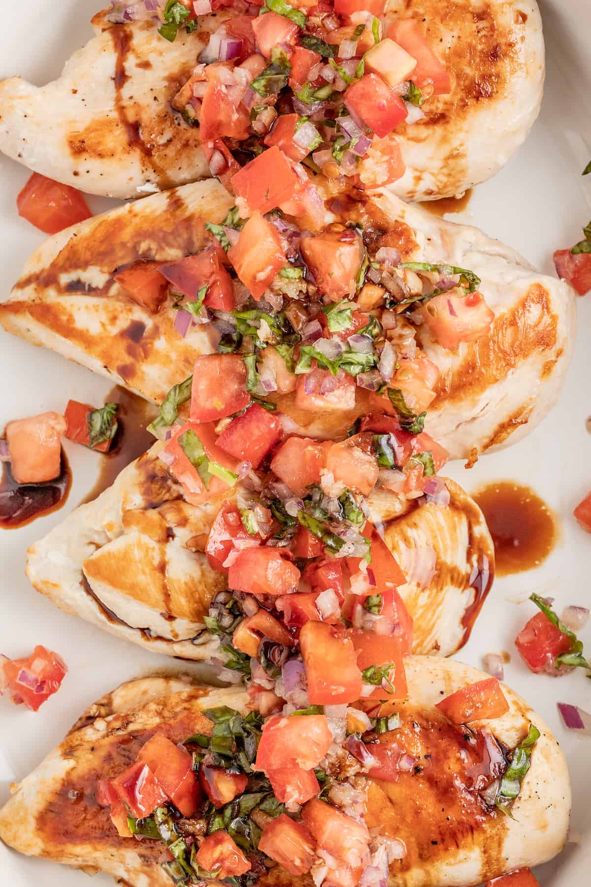 This juicy chicken bruschetta with an Italian-inspired summer veggie topping is the perfect 20-minute healthy but flavorful work lunch. Chicken bruschetta on a plate with a drizzle of balsamic reduction.