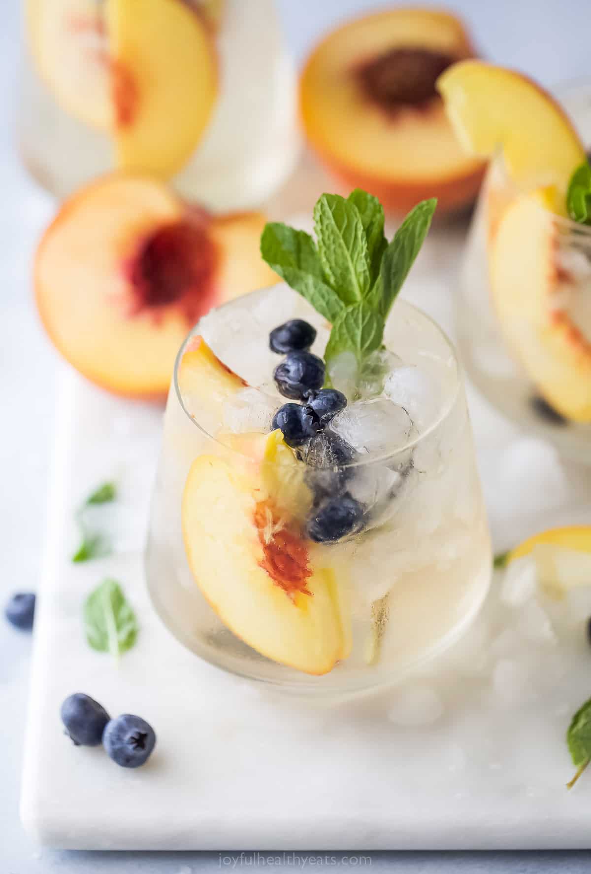 This icy peach sangria with blueberries, peach Schnapps, and mint is the fruity cocktail you'll be sipping on all summer. Peach sangria with mint in a crystal glass.