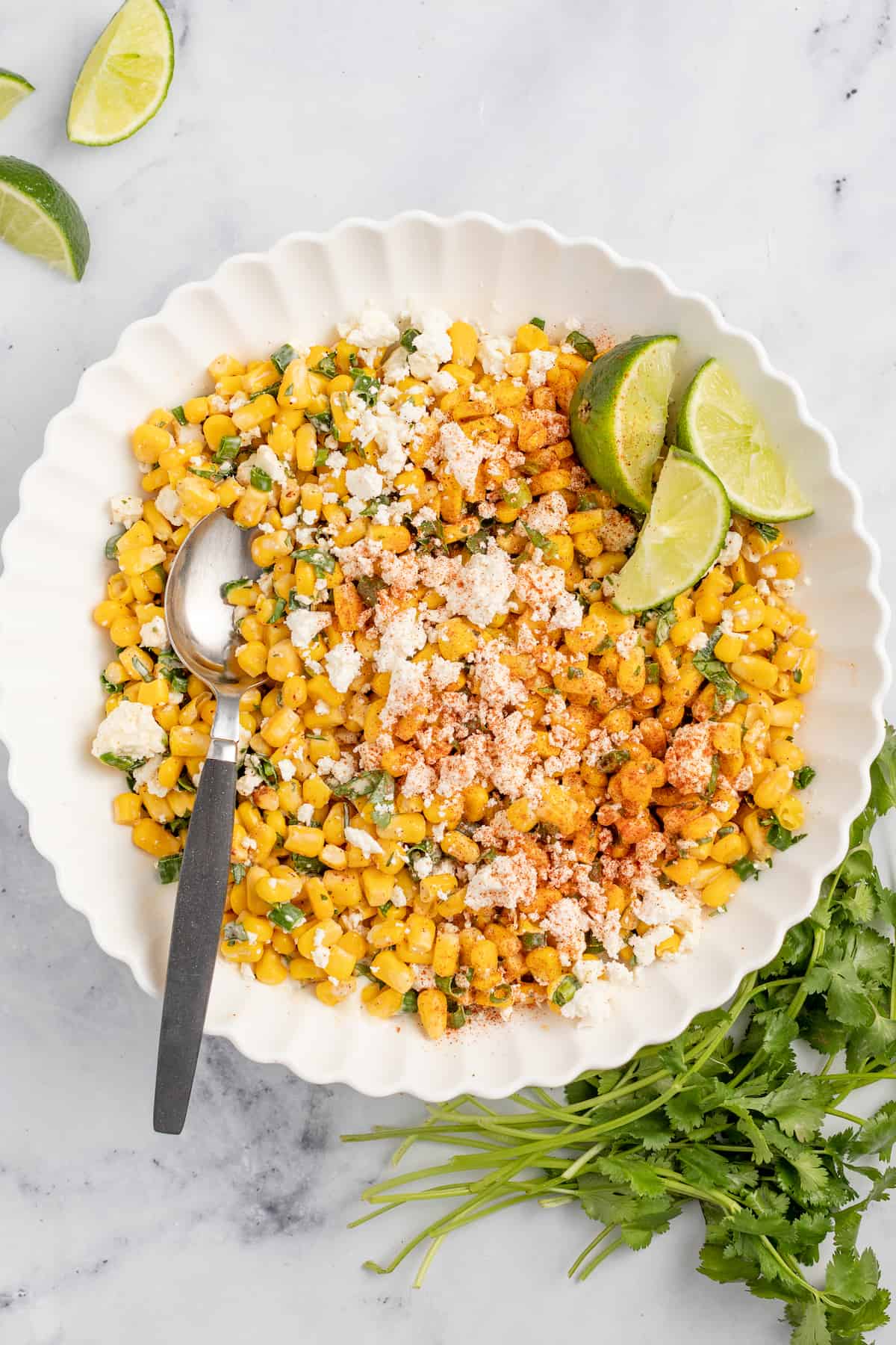 This 10-minute Mexican street corn dip is loaded with mayo, cotija cheese, lime juice, and chili powder for an authentic snack at home. Mexican street corn in a bowl with lime wedges on the side.