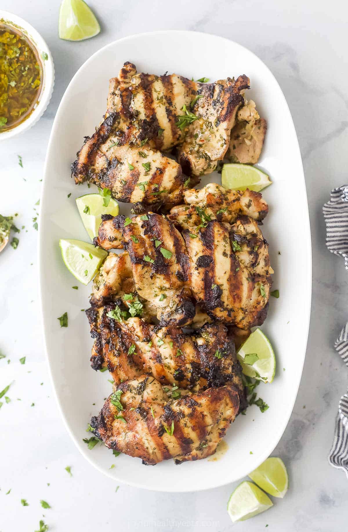 Topped with extra chimichurri, this juicy chimichurri chicken will be your new excuse to fire up the grill this summer. You'll love it! Chimichurri chicken on a plate with lime wedges.