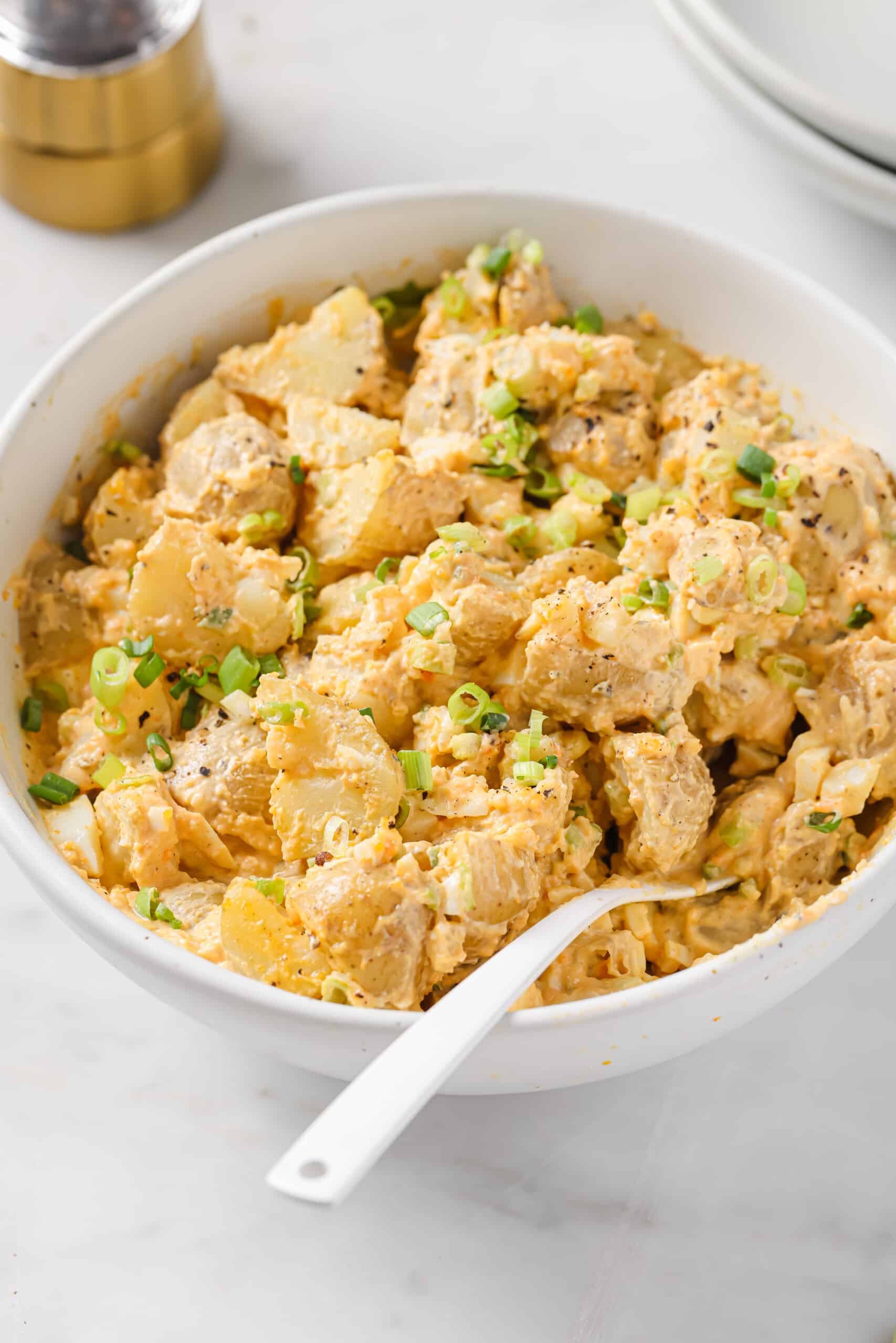 This easy deviled egg potato salad is creamy, tangy, and rich. Served chilled or warm, it'll be your new favorite summer side! Bowl of deviled egg potato salad with green onions.