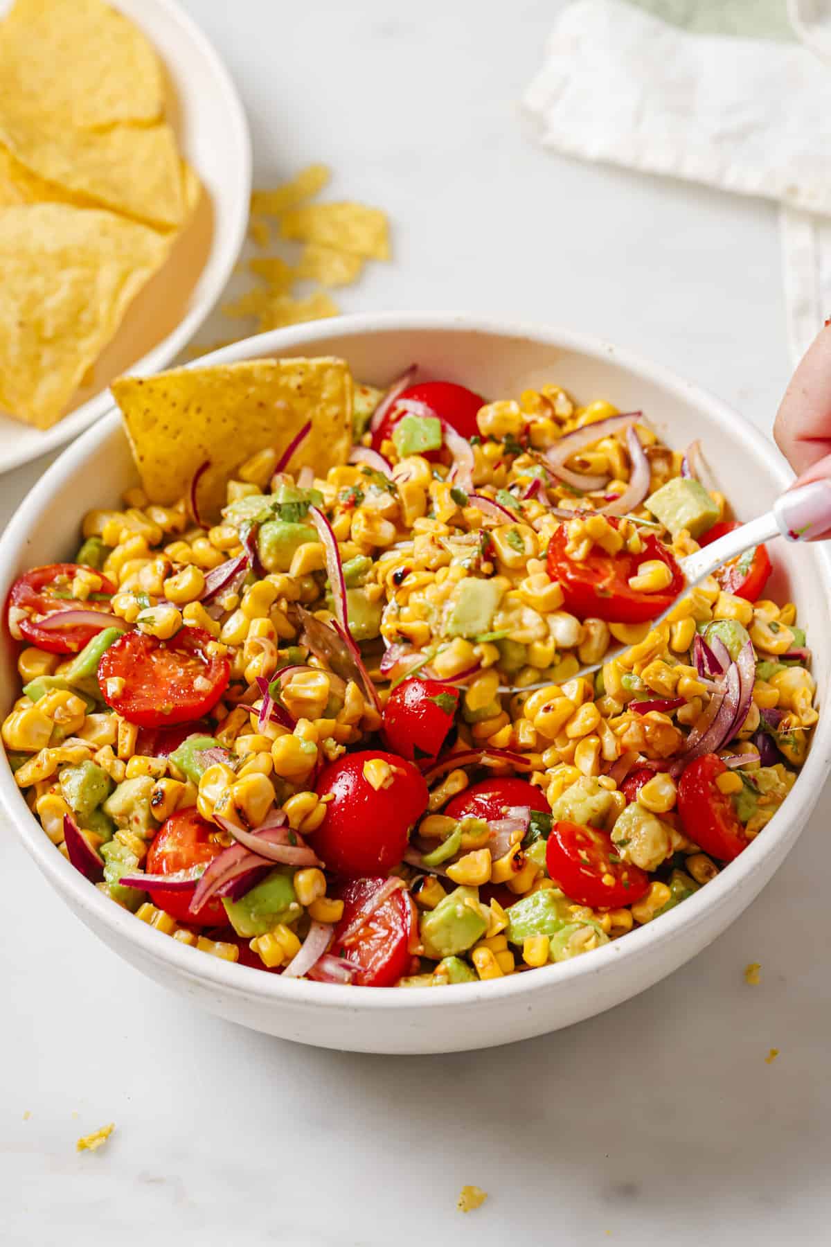 This easy avocado corn salad with a tangy honey dressing will find its way to your menu again and again. It's perfect! Bowl of avocado corn salad with corn chips.