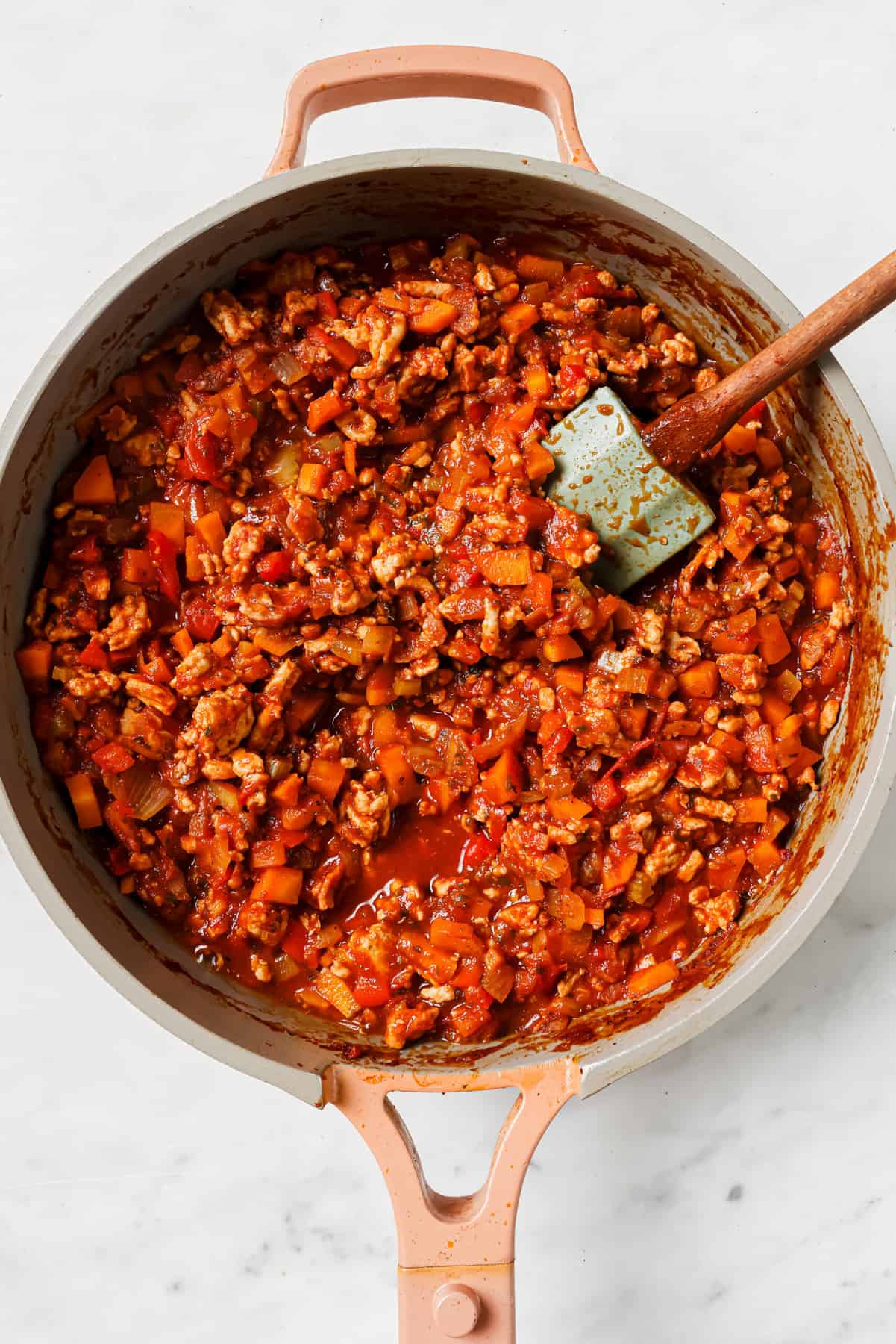 Mixing the sauce, ground turkey, veggies, and bacon in the pan.