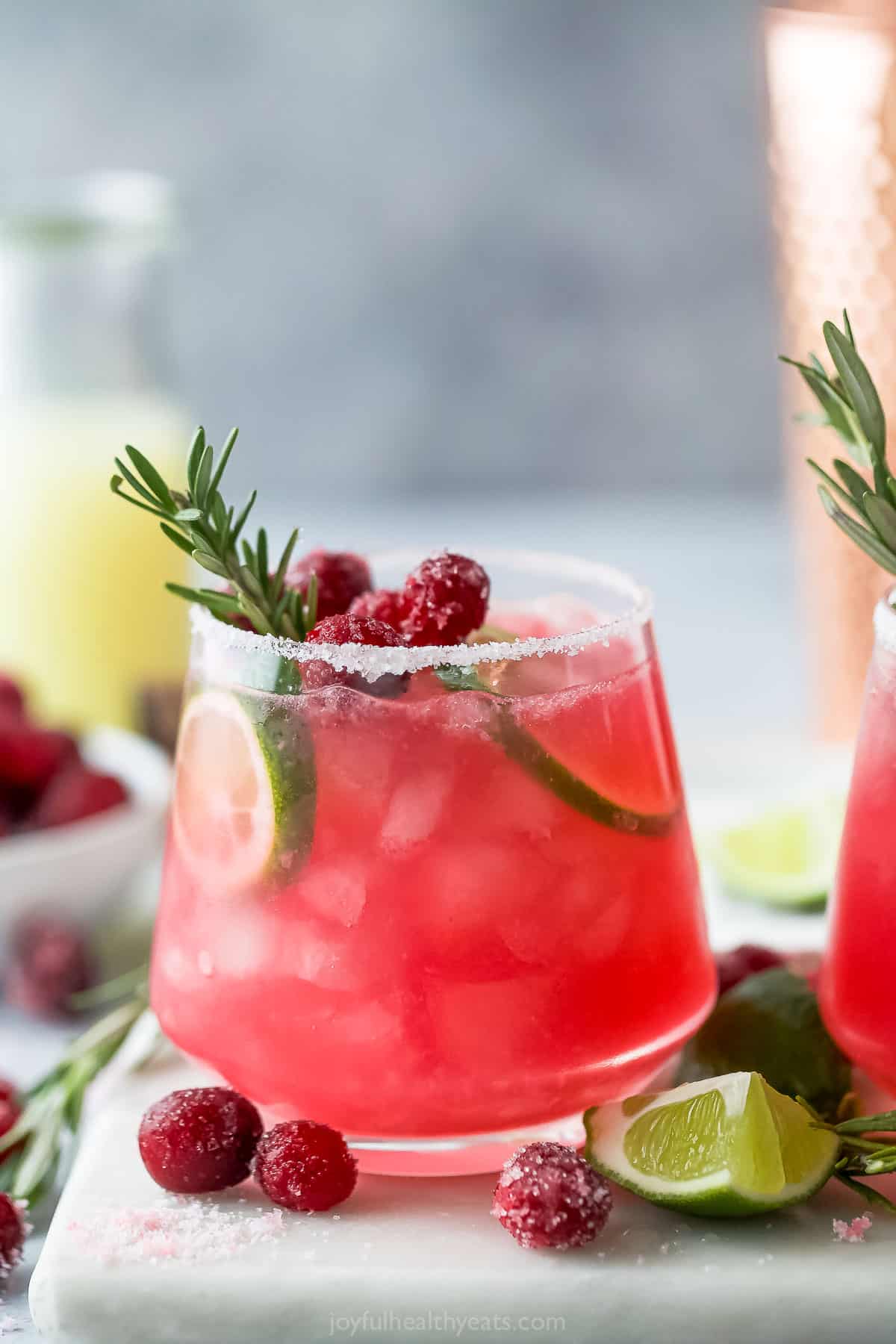This Mistletoe Margarita is a festive holiday cocktail made with cranberry juice, orange liquor, lime juice and tequila for the perfect sip. closeup of mistletoe margarita garnished with cranberry, lime and rosemary
