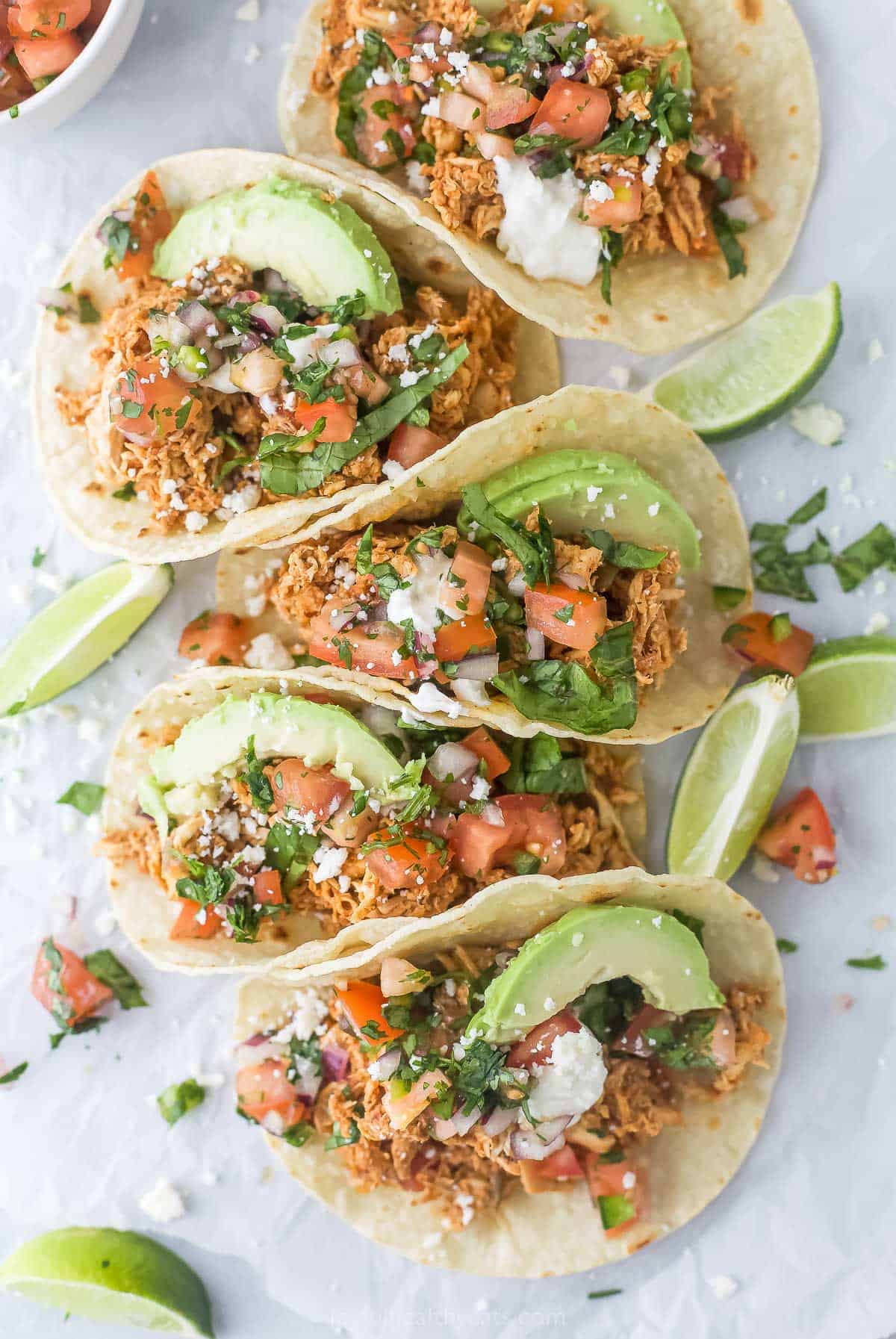 This smokey rotisserie chicken tacos recipe with chunky salsa, creamy avocado, and pico de gallo is a great dinner idea to use up leftovers. 5 rotisserie chicken tacos with pico de gallo and sliced avocado on top.