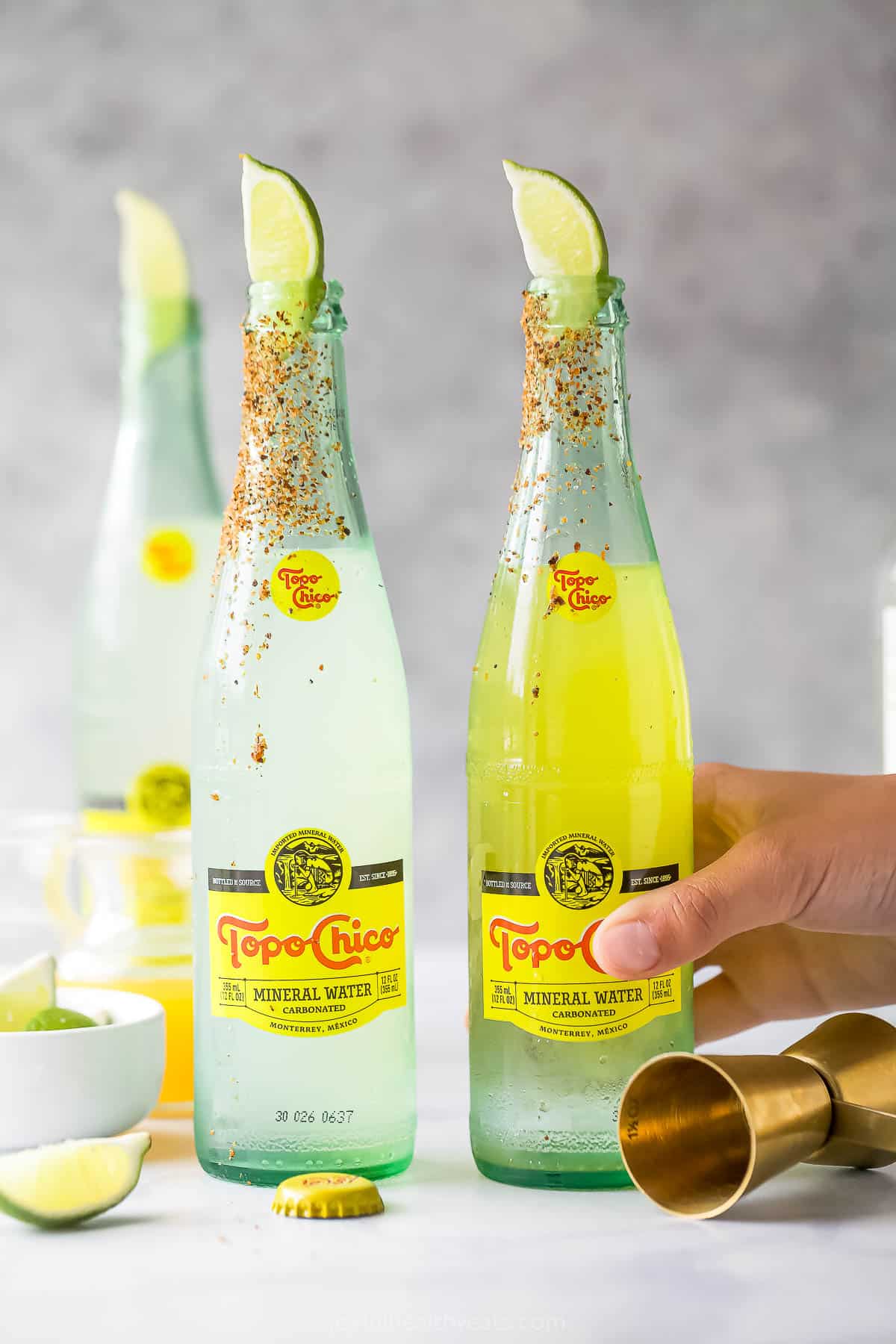 This sparkling ranch water recipe with sharp tequila, fruit juice, and Tajin rim is an easy 5-minute cocktail for the summer. Topo Chico bottles with a Tajin rim for the ranch water recipe.