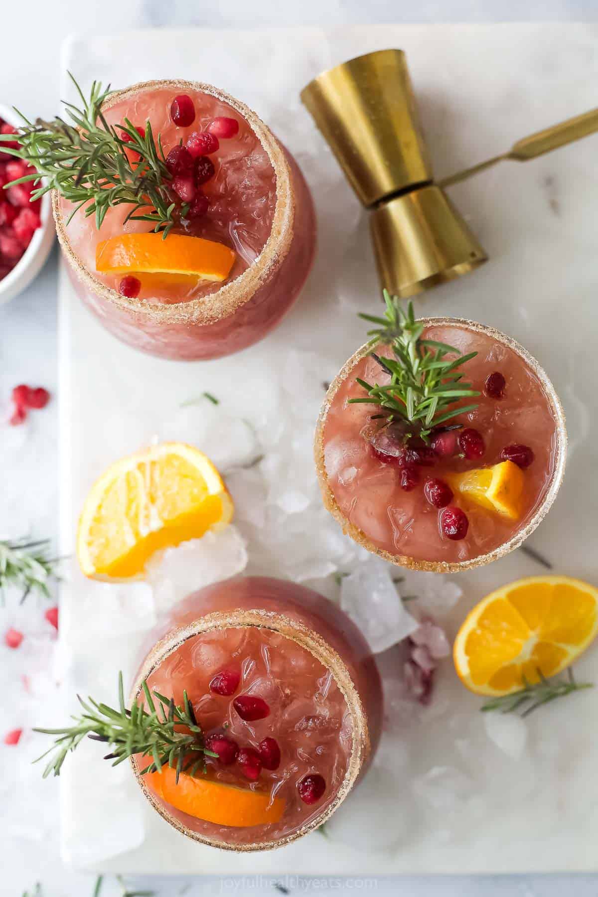 Several fruity cocktails with rosemary sprigs, pomegranate arils, and orange slices as garnishes. 