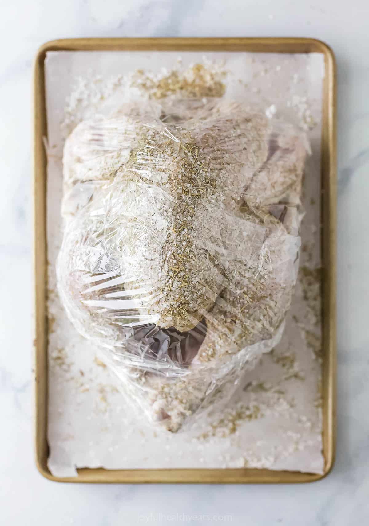 Wrapping the turkey in plastic wrap. 