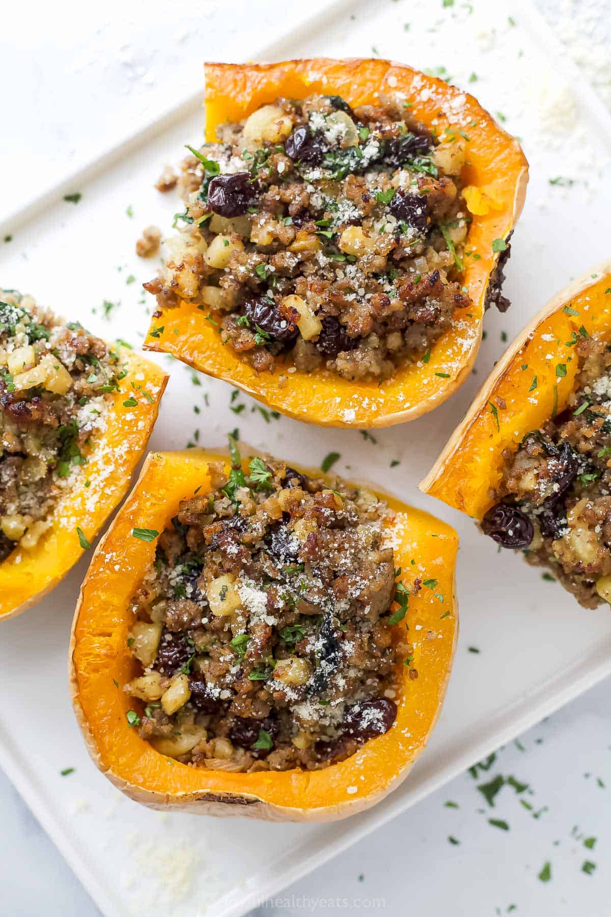 This sweet-and-savory stuffed butternut squash recipe with sautéed sausage-apple filling is an easy Thanksgiving side. Close-up of stuffed butternut squash with juicy sausage-apple and cherry filling inside.