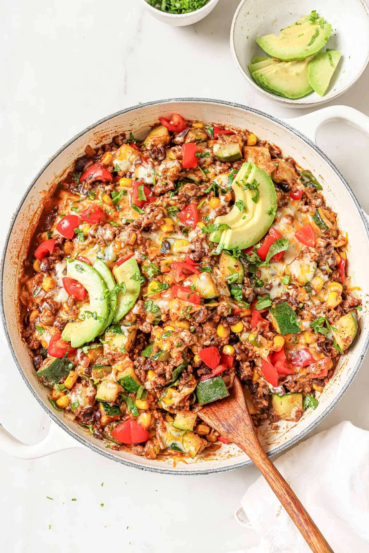 This garlicky ground beef and zucchini recipe with sweet onions, 2 types of peppers, and spicy enchilada sauce is a 30-minute dinner. Ground beef and zucchini recipe with melty cheese, avocado, and tomatoes on top.