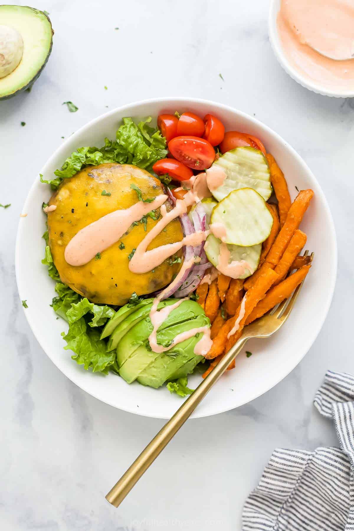 This hearty burger bowl recipe with fresh veggies, sweet potato fries, and special burger sauce is an easy 25-minute dinner. Assembled burger bowl recipe with special mayo-ketchup sauce drizzled on top.