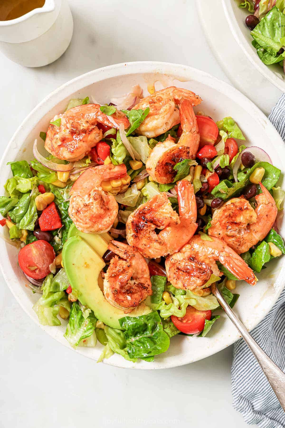 This chipotle grilled shrimp salad recipe with Tex-Mex flair and homemade lime-honey dressing is an easy weeknight dinner. A bowl of grilled shrimp salad with creamy avocado, beans, and juicy tomatoes.