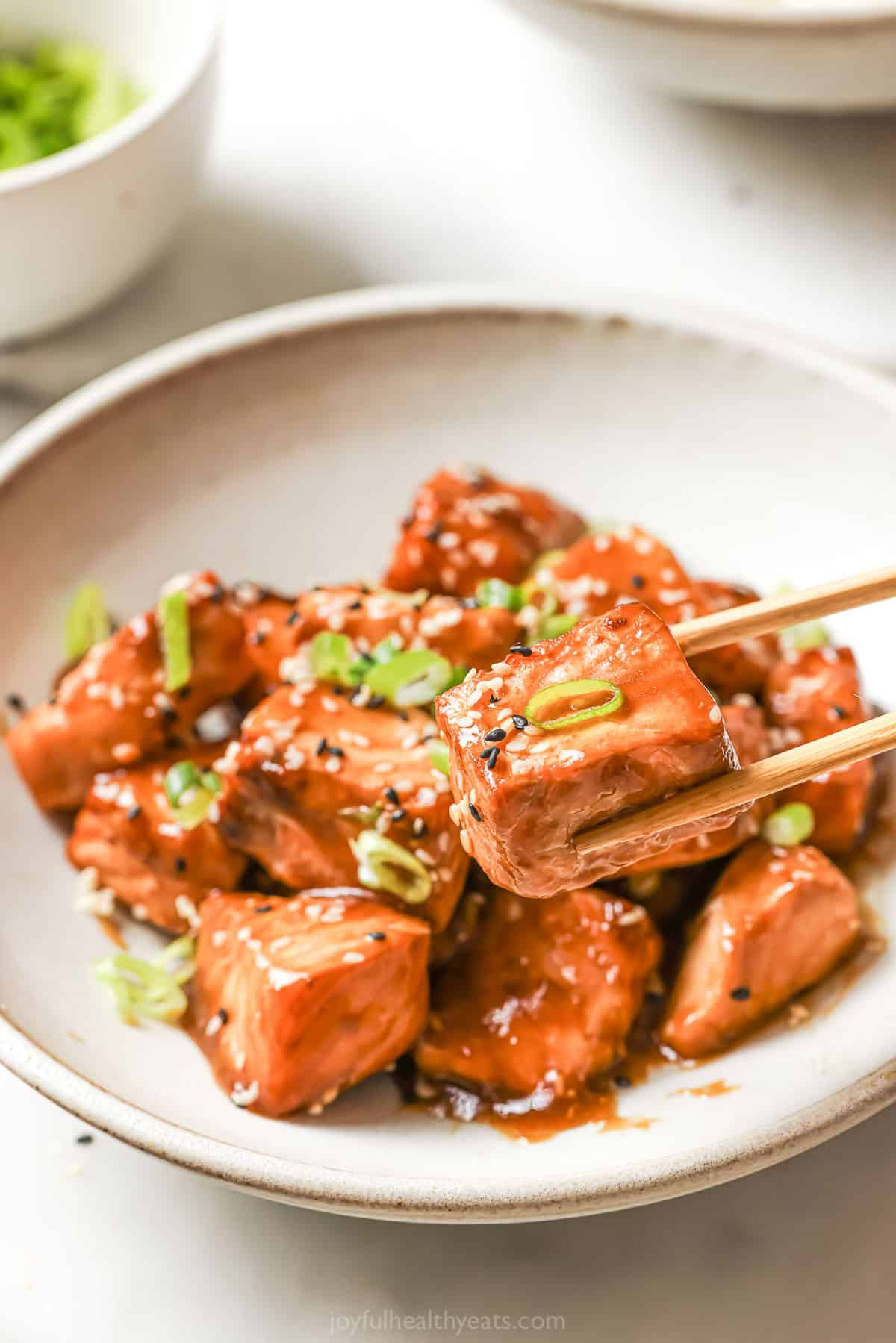 Lifting salmon bite from bowl with chopsticks
