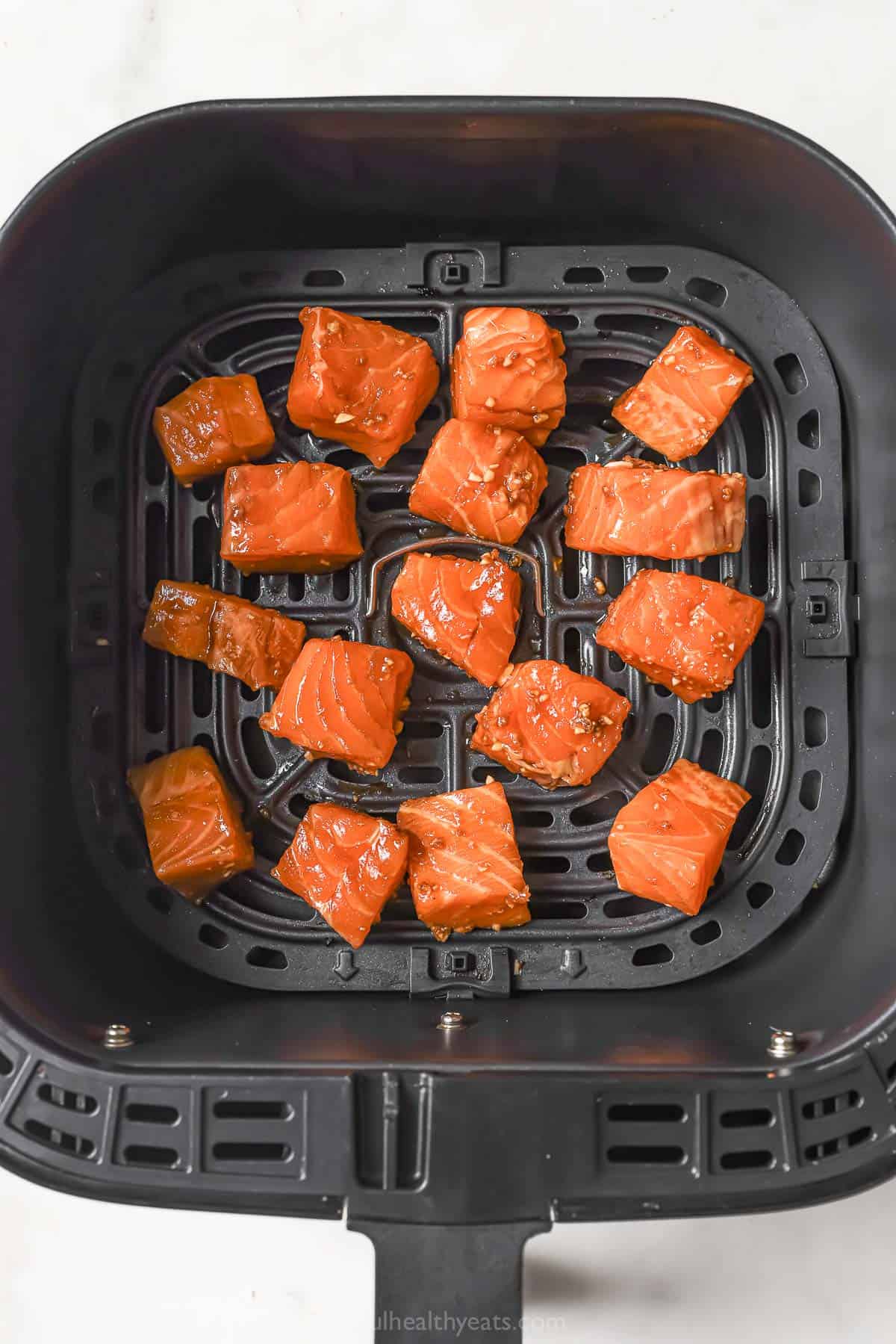 Uncooked salmon cubes in air fryer basket