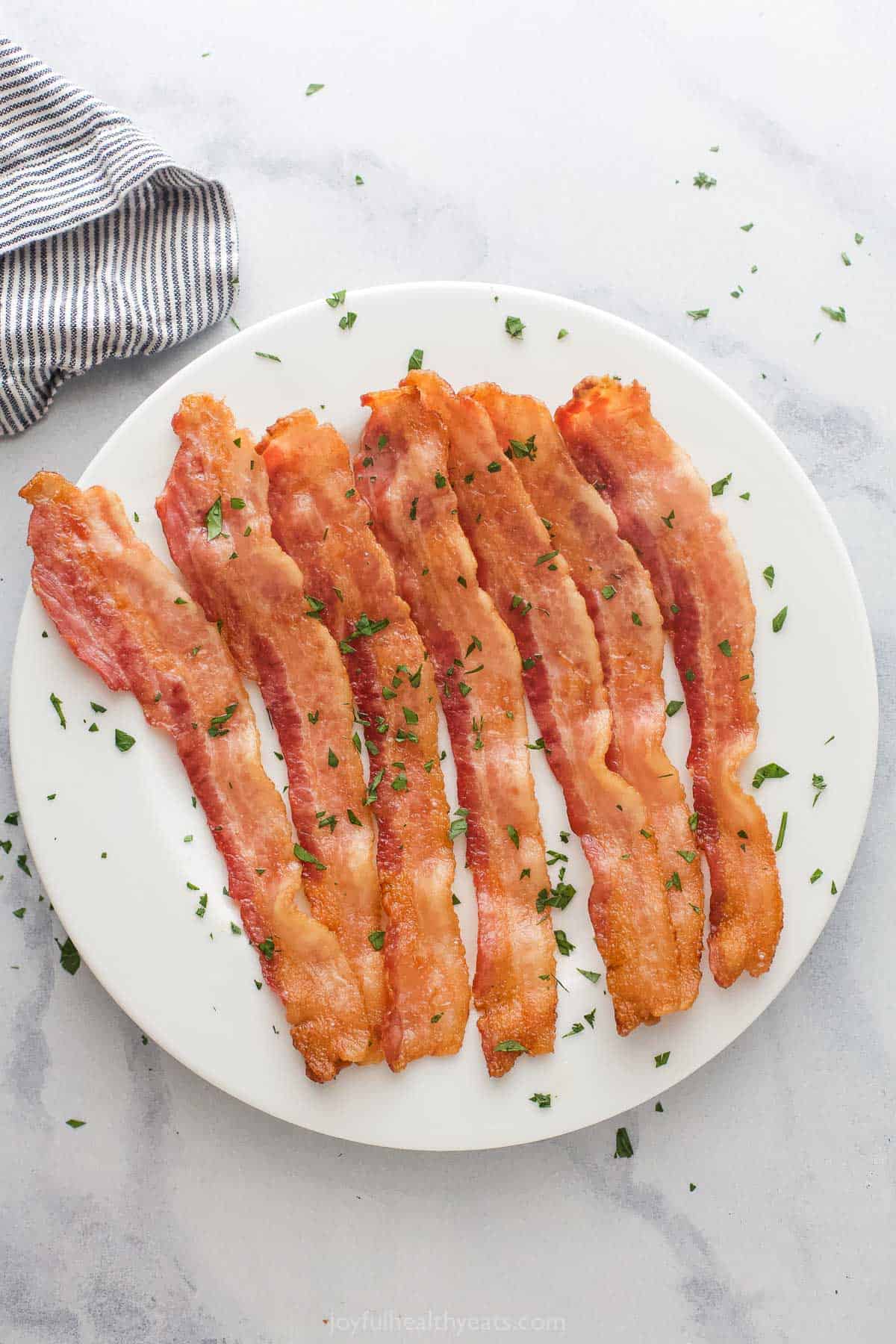 This crispy baked bacon recipe is the perfect way to prepare lots of your favorite breakfast side at the same time. Baked bacon on a serving plate.