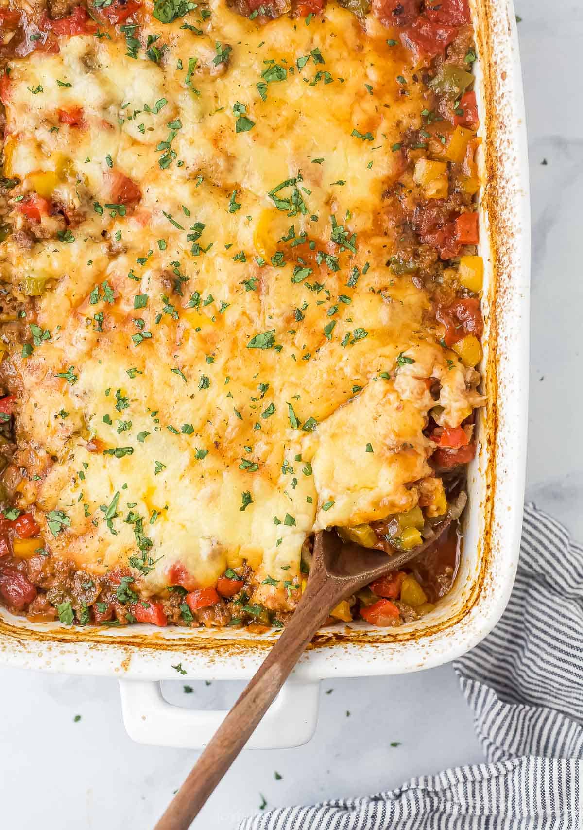 This comforting stuffed pepper casserole recipe with lots of tomatoes, herbs, and onions is an Italian-inspired weeknight dinner. Close-up of the stuffed pepper casserole with melty cheese and fresh parsley on top.