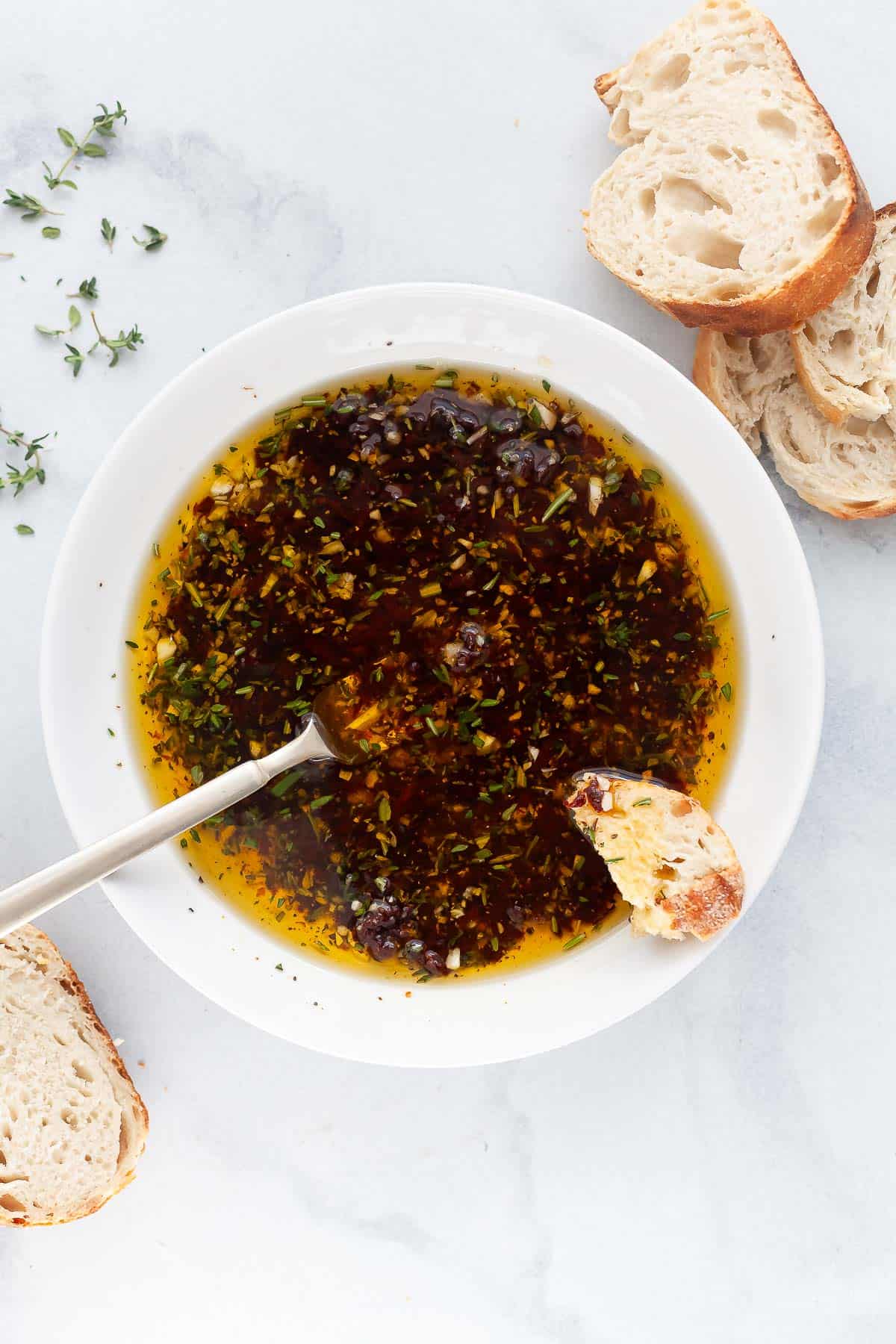 Bread dipping oil makes any meal into a restaurant-style dinner! My recipe is made with fresh herbs, sun-dried tomatoes, and garlic. Yum! Overhead view of bread dipping oil in bowl with spoon