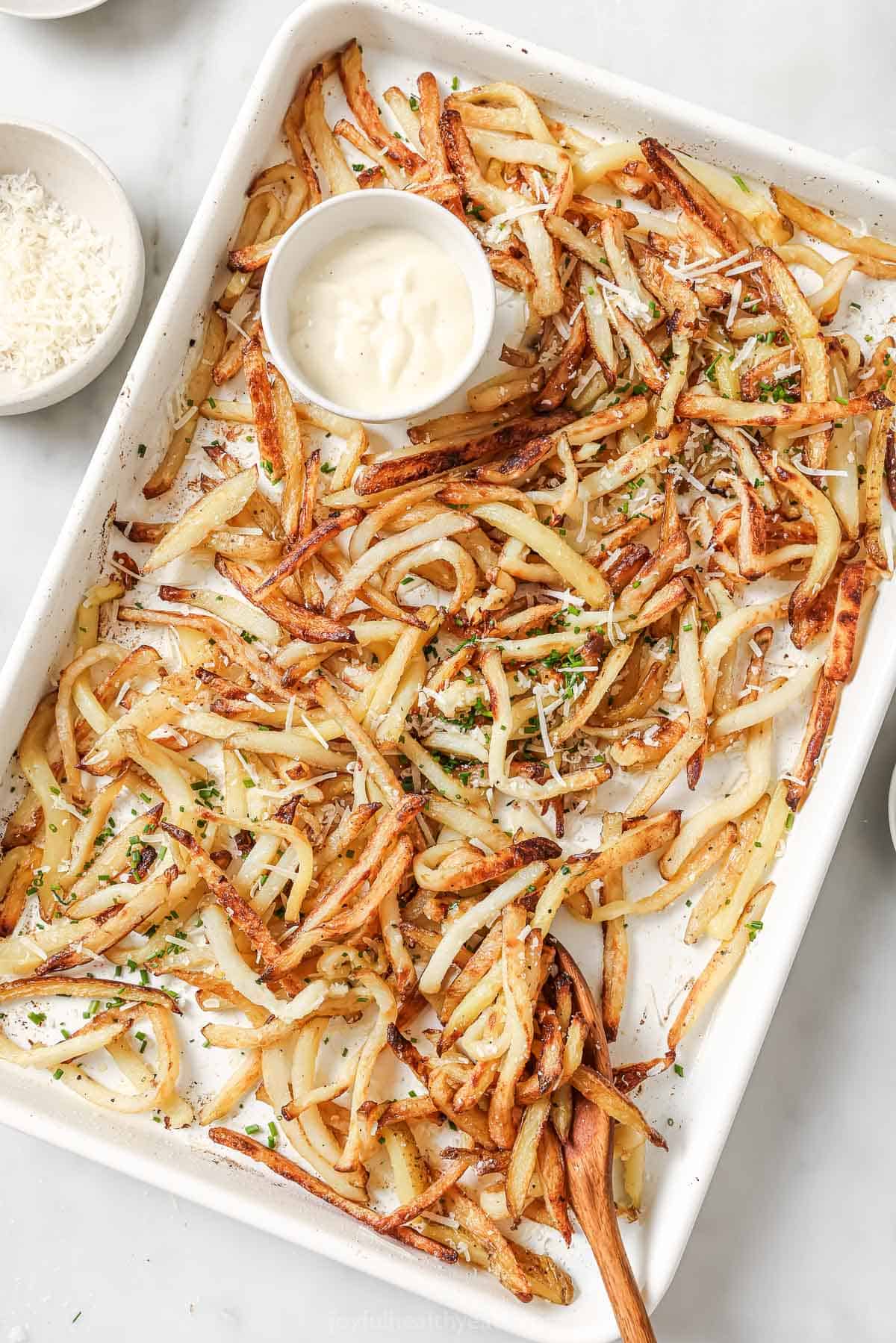 Overhead view of Parmesan truffle fries on pan with bowl of aioli