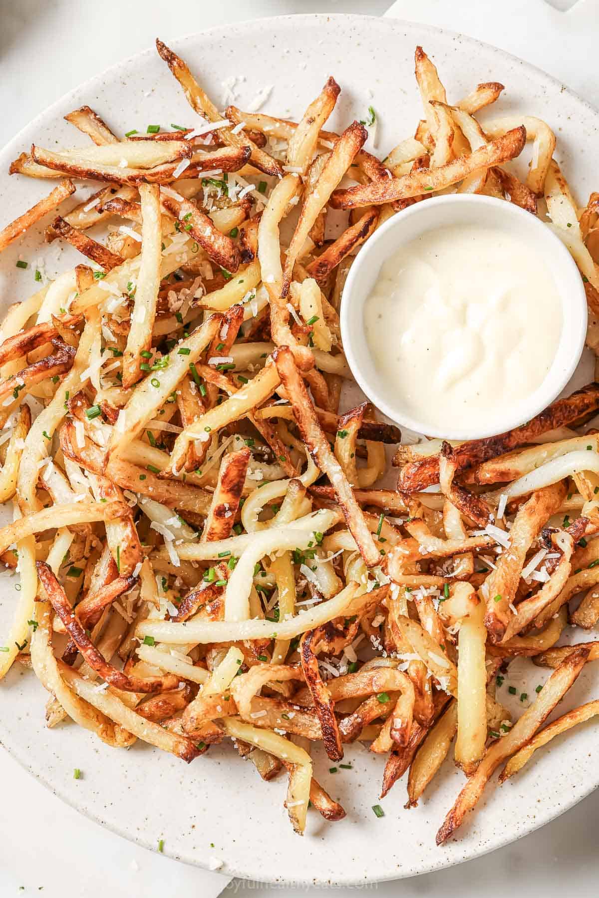 Overhead view of Parmesan truffle fries on plate with small bowl of aioli