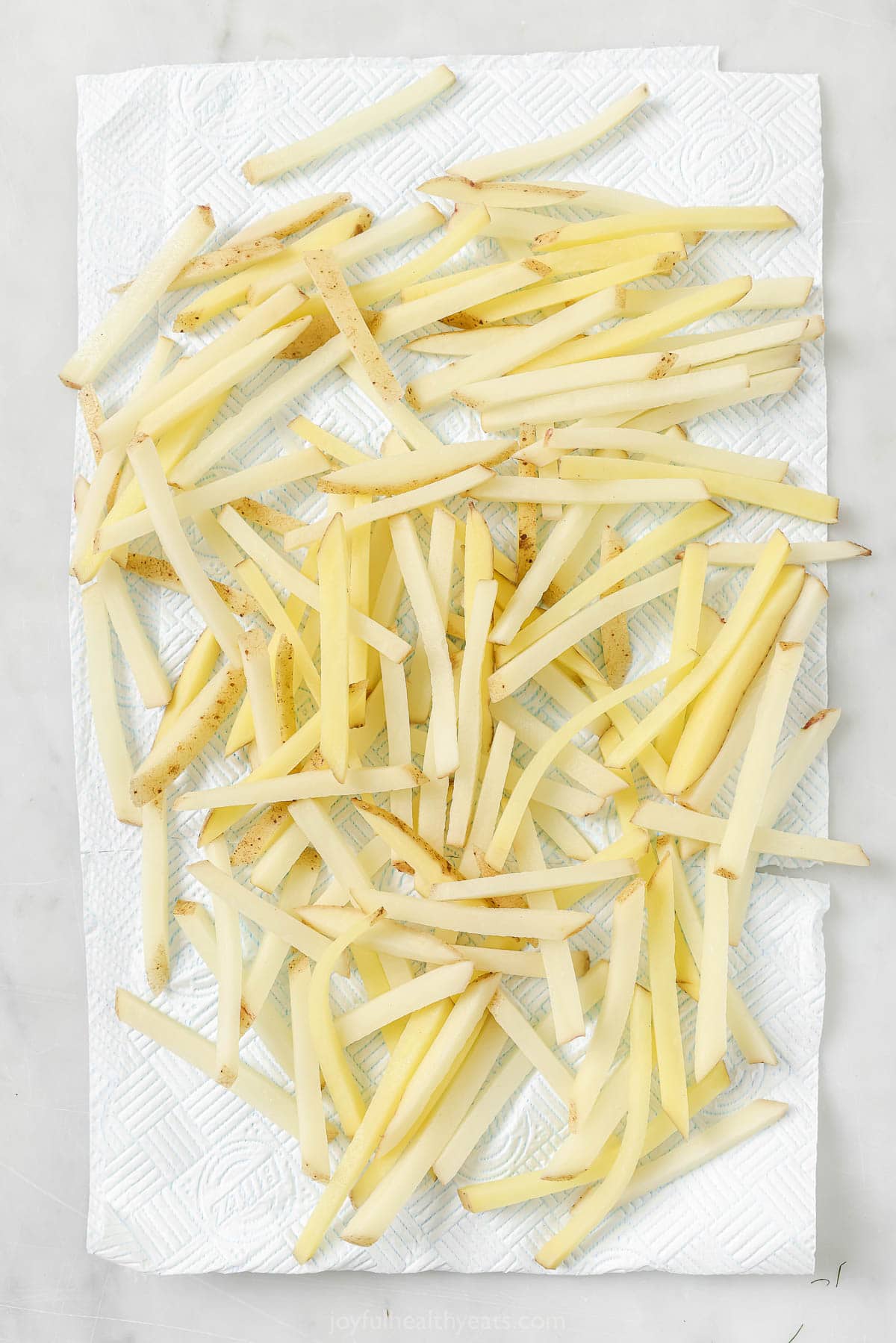 Overhead view of cut fries draining on paper towels after soaking in water