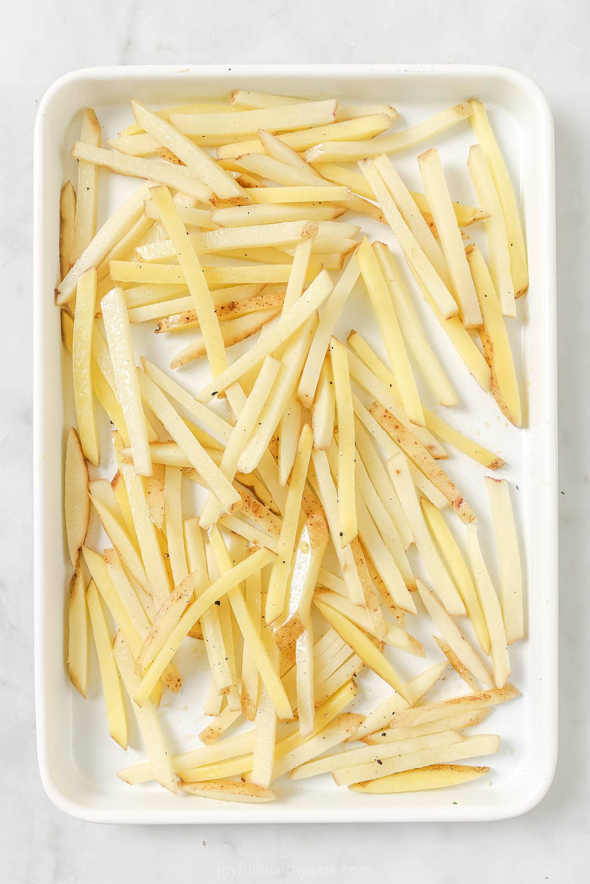 Overhead view of unbaked fries on sheet pan
