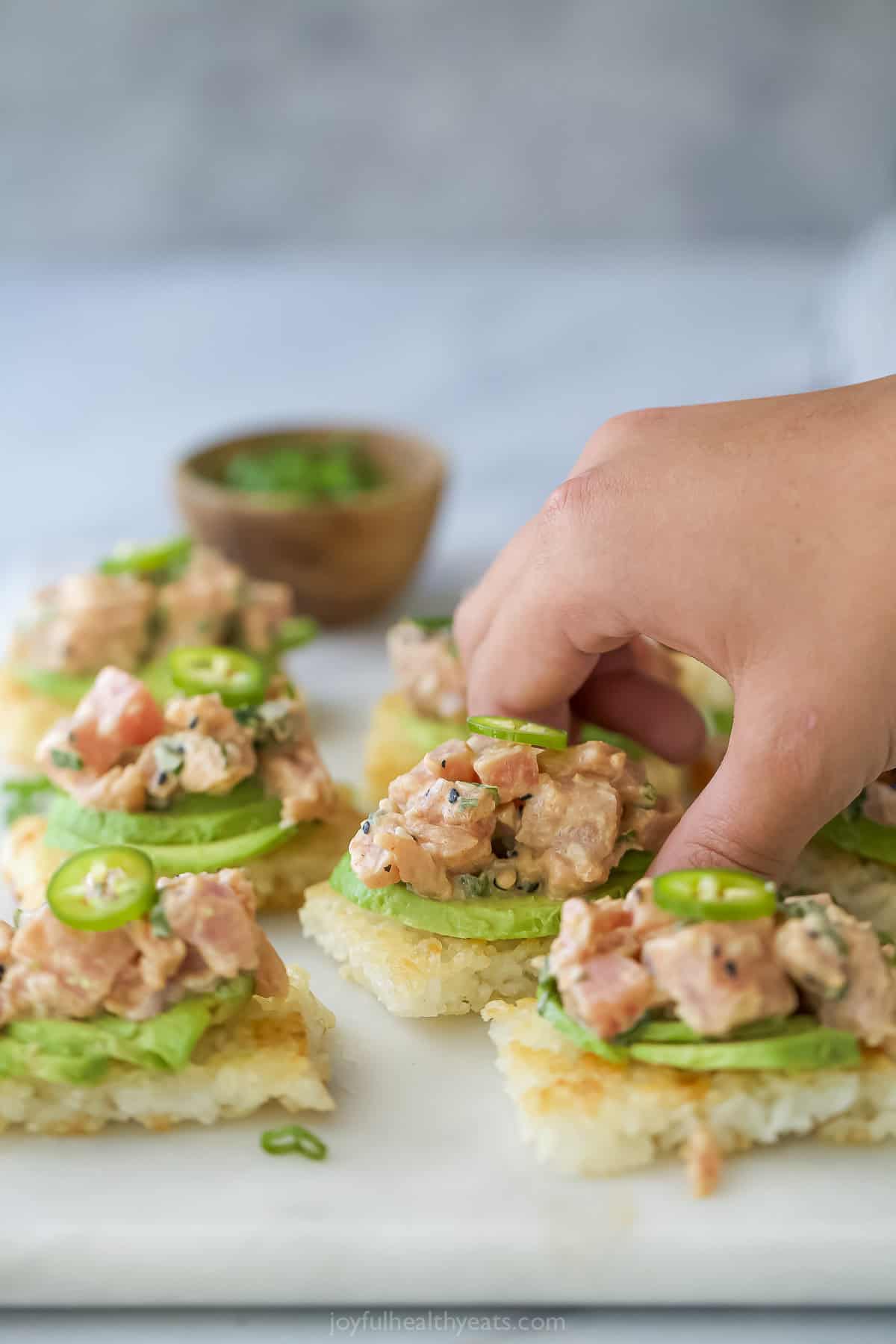 Hand grabbing spicy tuna crispy rice bite from board